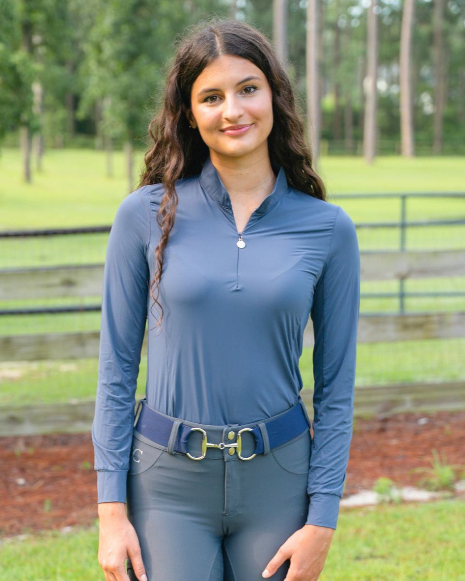 Woman wearing a blue equestrian top and gray pants in an outdoor setting